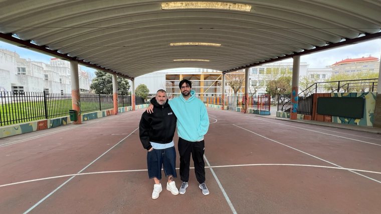 Patio cubierto del colegio La Normal con Miguel y otra persona abrazados; las columnas y los muros están pintados con animales y plantas