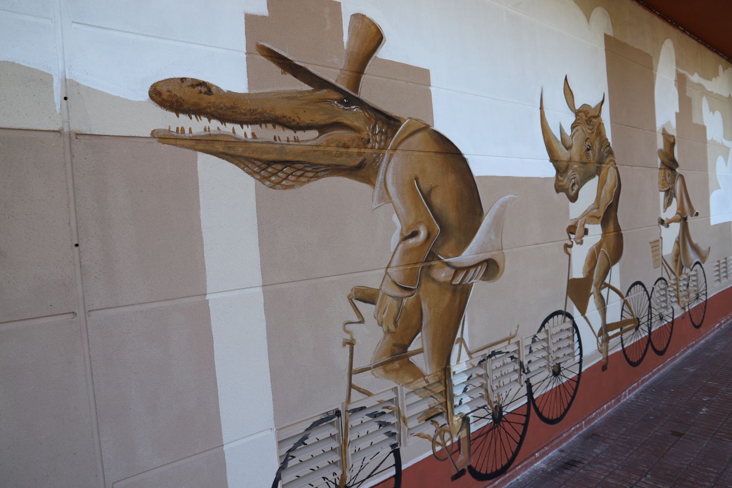 Paseo en bicicleta: mural en tonos sepia con un cocodrilo con sombrero de copa, un rinoceronte y un armadillo montados en bicicletas