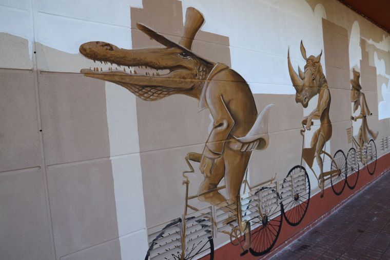 Paseo en bicicleta: mural en tonos sepia con un cocodrilo con sombrero de copa, un rinoceronte y un armadillo montados en bicicletas
