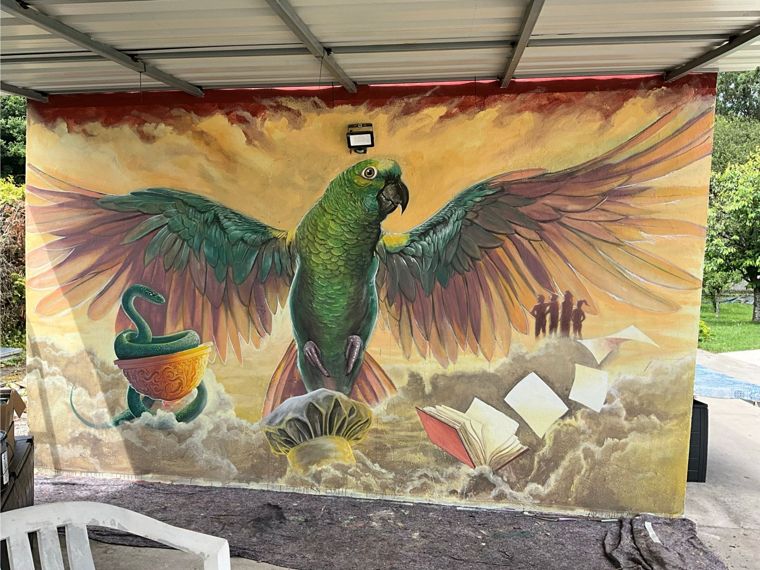 Tarzán: mural de un loro verde con las alas abiertas sobre un mar de nubes, con una serpiente enroscada en una copa, un libro abierto y cuatro siluetas