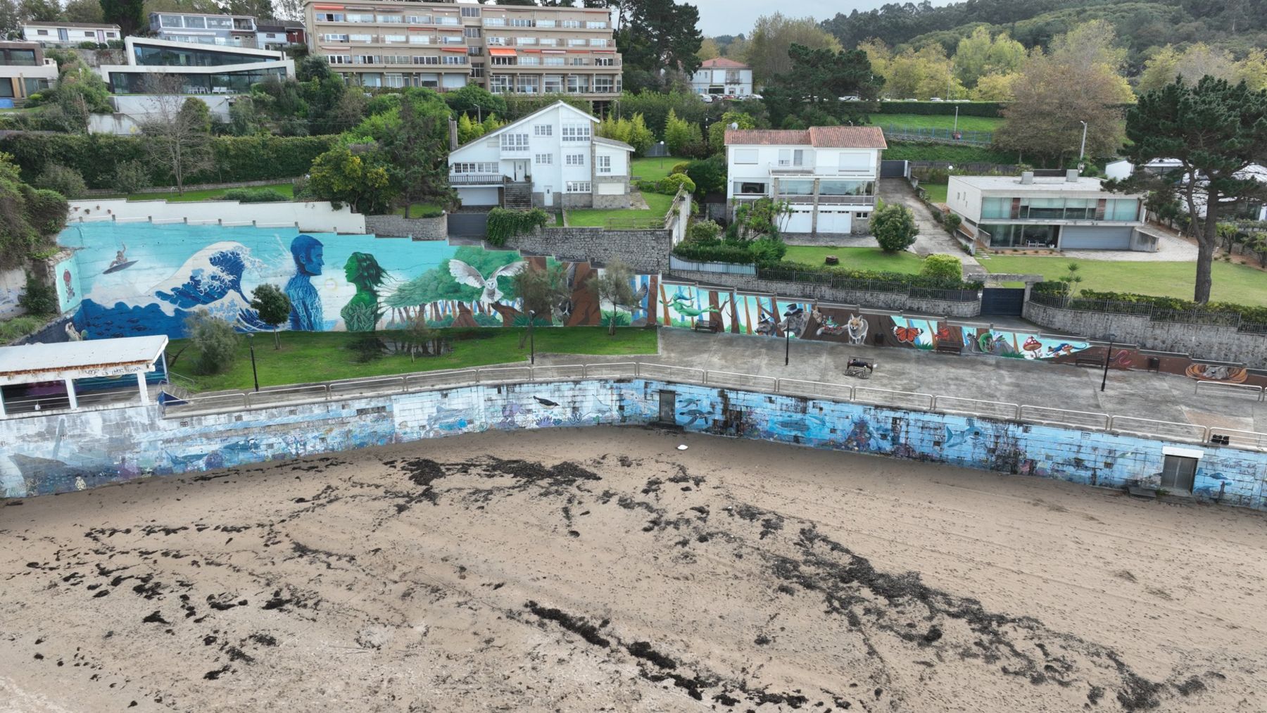 Turquesa: mural en el muro de la playa de Bastiagueiro, con una gran ola, un hombre azul y una mujer verde frente a frente, una lechuza y un bosque con animales